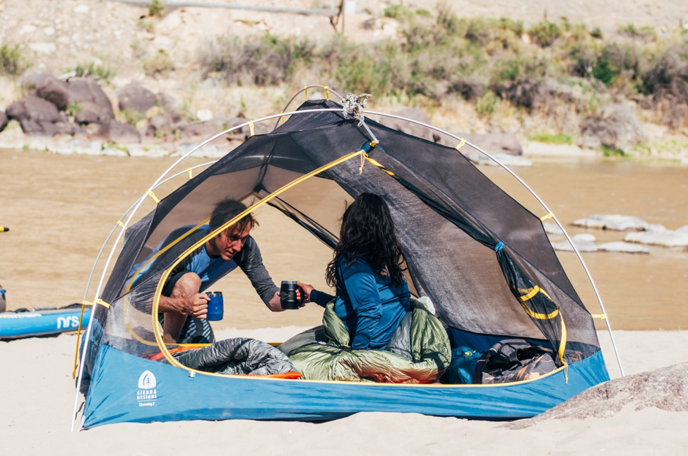 A picture of two people in a tent next to a river